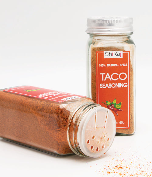 Two clear plastic spice jars of ShiRaj Taco Seasoning on a white background, with one jar lying on its side showing the shaker top and the other standing upright showing the red label.